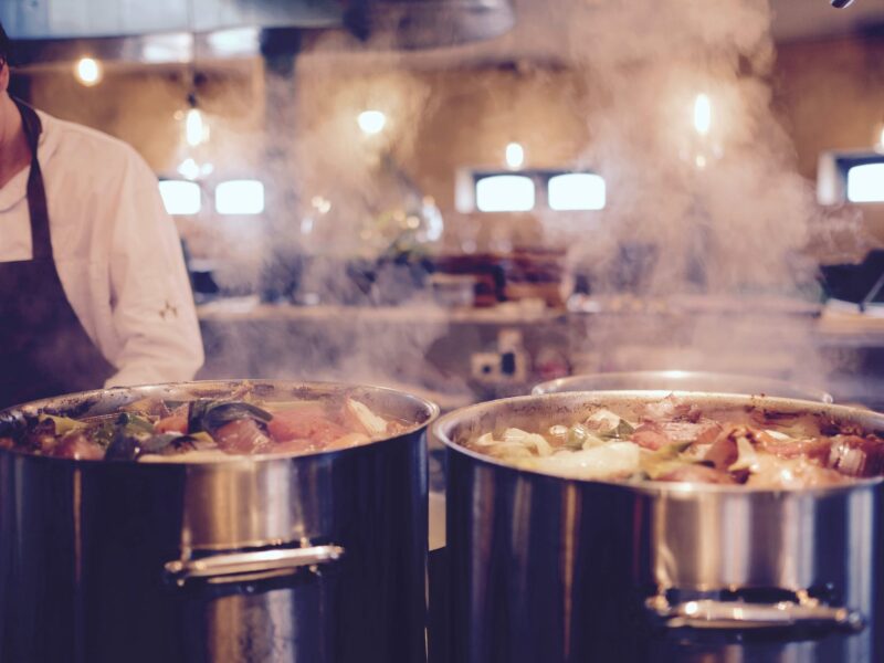 man wearing black apron near two silver metal cooking pot