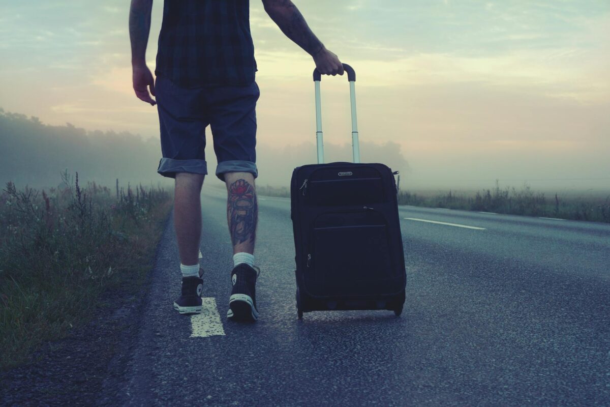 man walking on the road holding black luggage during sunset