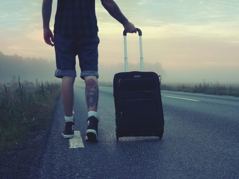 man walking on the road holding black luggage during sunset